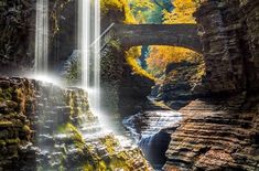 a waterfall with a bridge over it in the middle of fall colors and green mossy trees