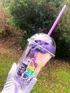 a person in white gloves holding up a cup with purple straws and butterflies on it