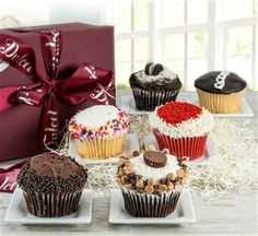 four cupcakes with different toppings are on plates next to a gift box