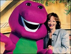 a woman standing next to a large purple dinosaur mascot in front of a building with trees