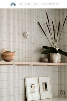 two framed pictures are sitting on a shelf above a sink in a bathroom with white tile