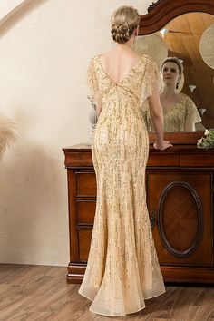 a woman standing in front of a mirror looking at herself in the mirror wearing a gold dress