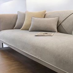 a couch with several pillows on it in front of a wall and wooden flooring