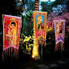 there are three banners hanging on the pole in front of some trees and bushes, one has an image of jesus