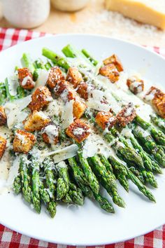 a white plate topped with asparagus covered in parmesan cheese and sauce