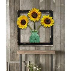 three sunflowers are in a vase on a table next to a wooden wall