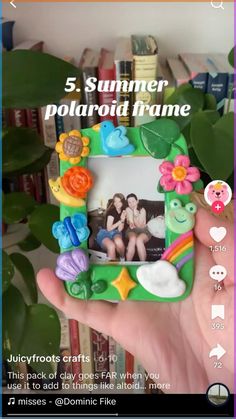 a person holding up a small photo frame with flowers and hearts on it, in front of bookshelves