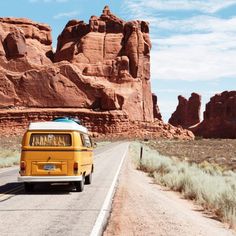 a yellow van is driving down the road in front of some red rocks and grass