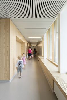 two children walking down a long hallway with wood slats on the ceiling and white walls