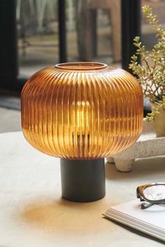 a glass lamp sitting on top of a table next to a book and eyeglasses