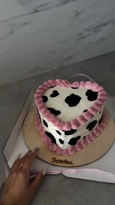 a heart shaped cake with pink icing and black spots on the top is being cut