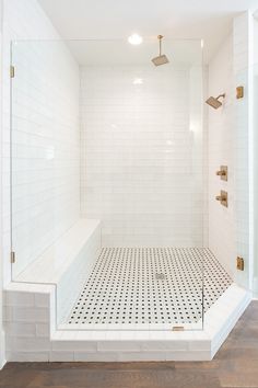 a white tiled shower with gold fixtures and wood flooring