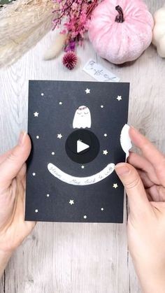 two hands holding up a black card with an owl on it and stars in the sky