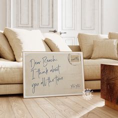 a sign sitting on top of a wooden floor next to a couch with pillows and throw pillows