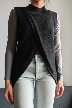 a woman standing in front of a gray couch wearing jeans and a black sweater with an asymmetrical design