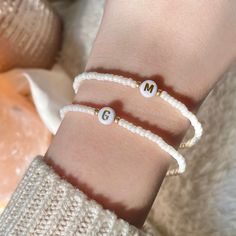 two white bracelets with gold beads and the letter m on each one is personalized