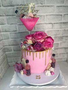 a pink and gold birthday cake with flowers on top, next to a bottle of booze