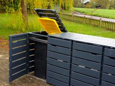 a large black box with yellow lid sitting in the middle of a brick walkway next to a green field