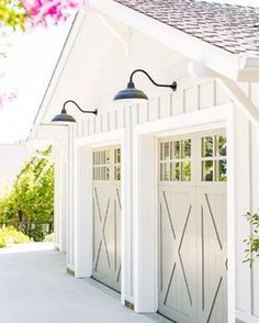 two garage doors are open on the side of a white house with pink flowers in front