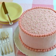 a pink cake sitting on top of a table next to plates and silverware,