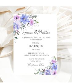 a white and blue floral wedding card with purple flowers on the front, in watercolor