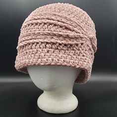 a white mannequin head wearing a pink crochet hat on a black background