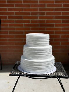 a large white cake sitting on top of a metal rack next to a brick wall