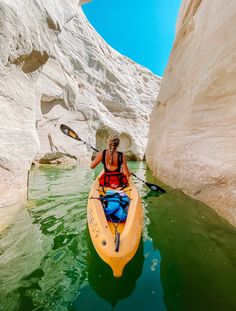 a woman in a kayak paddles through the water between two large white cliffs