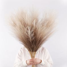 a woman holding a bunch of dry grass in front of her face