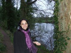 a woman standing next to a tree near a body of water