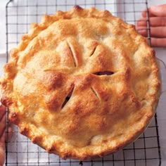 a pie sitting on top of a cooling rack next to a person's hand