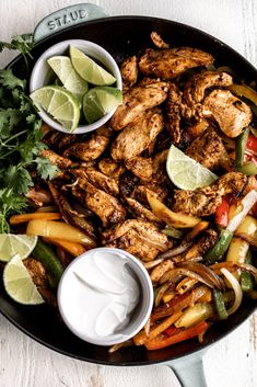 a skillet filled with chicken, peppers, onions and limes next to sour cream