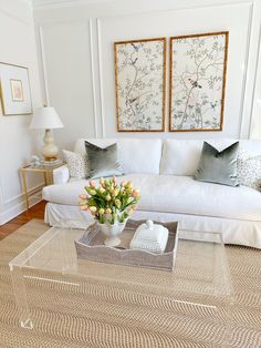 a living room with white couches and flowers on the coffee table in front of it