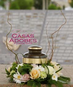 a vase with flowers and greenery sitting on the ground next to a sign that says cassas adobes flower shop