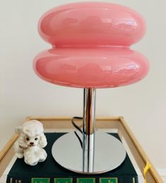 a pink lamp sitting on top of a table next to a small white teddy bear