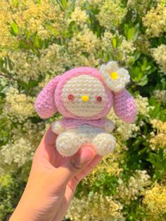 a hand is holding a small crocheted stuffed animal in front of some flowers