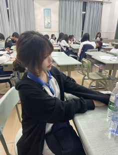 a woman sitting at a table in front of a bottle of water with another person behind her