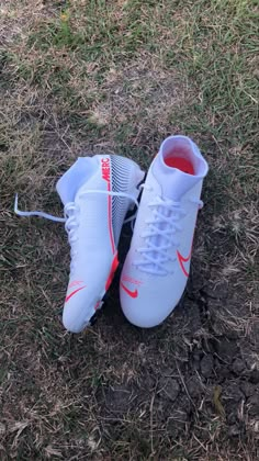 a pair of white and red nike soccer shoes on the ground with grass in the background