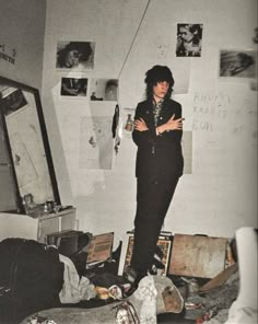 a man standing in a messy room with his arms crossed