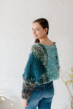 a woman standing in front of a white wall wearing a green and blue knitted sweater