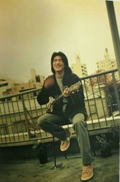 a man sitting on top of a metal chair holding a guitar in his right hand