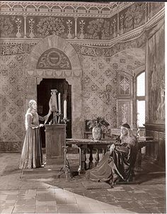 an old photo of two people sitting at a table in a room with ornate wallpaper