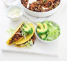 two tacos with lettuce, avocado and sour cream on the side