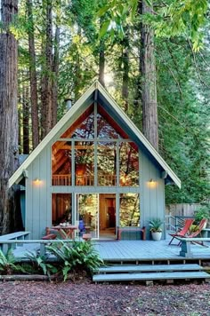 a small cabin in the woods with lots of trees and chairs on the front porch