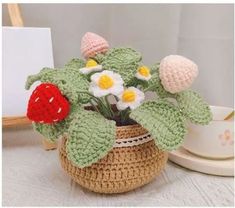 a crocheted planter with flowers in it on a table next to a cup