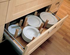 an open drawer in a kitchen filled with plates and bowls on top of wooden flooring