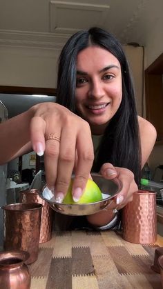 a woman sitting at a table with copper cups and an apple in front of her