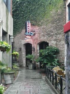 an alley way with potted plants on either side and a neon sign above the door