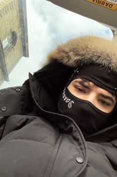 a man wearing a ski mask while standing in front of a window with a sky background