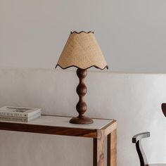 a lamp sitting on top of a wooden table next to a white wall and chair